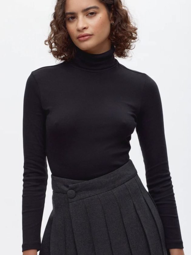 Model wearing black cotton turtleneck and wool pleated skirt