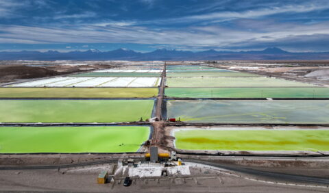 A view over green-coloured evaporation ponds to extract lithium with mountains in the background