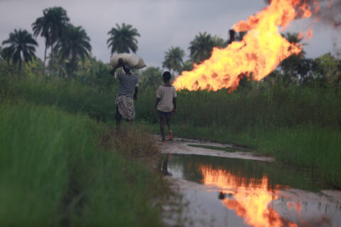 A boy follows a woman carrying a sack on her head as they walk towards a burning gas flaring furnace at a flow station in Ughelli, Delta State, Nigeria