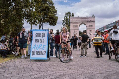 Cyclists and pedestrians pictured by a sign asking "Do you know what's in the air you breathe?" in Bogotá, Colombia