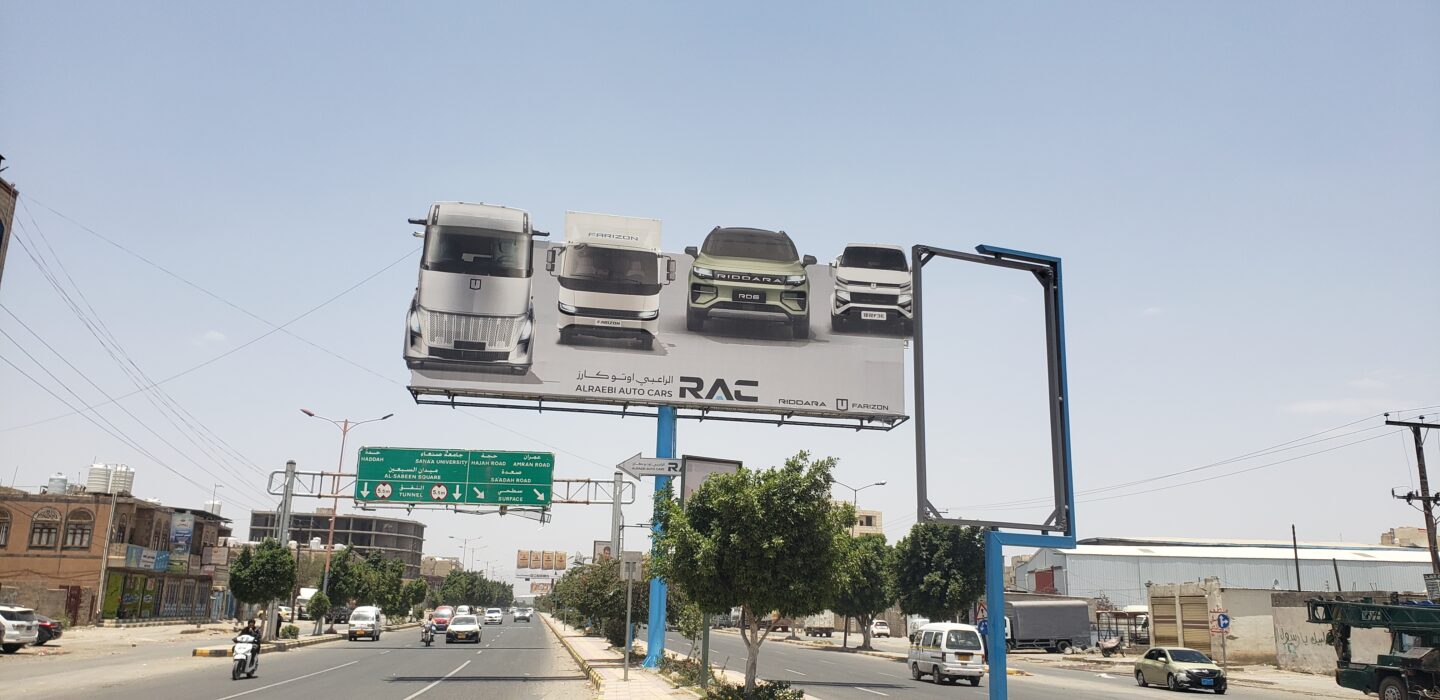 A billboard advertising electric car and truck models over a large avenue in Sanaa, Yemen