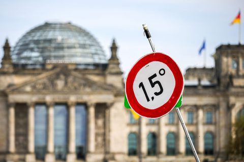 A demonstrator holds a banner showing the 1.5 degree Celsius mark, as protestors march past the Reichstag building calling for renewable energy on April 18, 2026 in Berlin, Germany