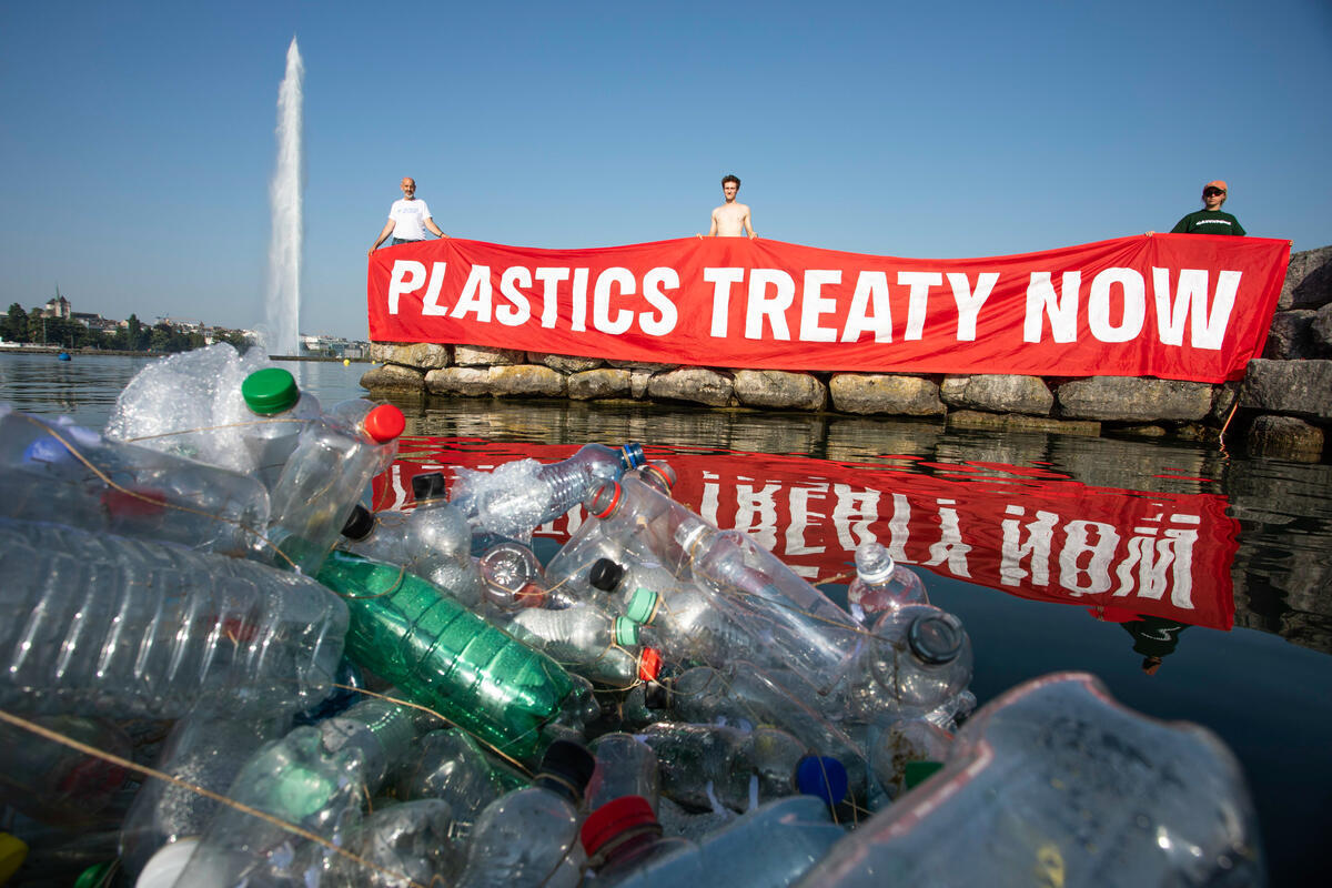 Plastics Treaty Now Banner at INC5 Activists hold up a banner saying "Plastics Treaty Now" in front of the Jet d'Eau of Geneva.