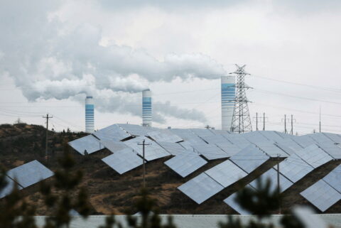 Smoke rises from chimneys near solar panels,