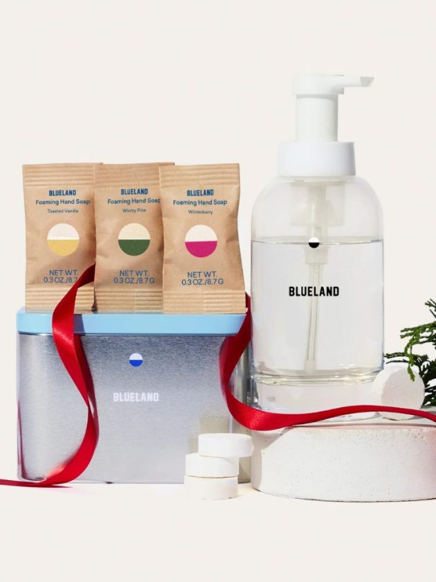 A styled pack shot of a plastic-free hand soap dispenser, with three refillable scented soap tablets next to it placed over a resuable tin, Blueland refillable hand soaps