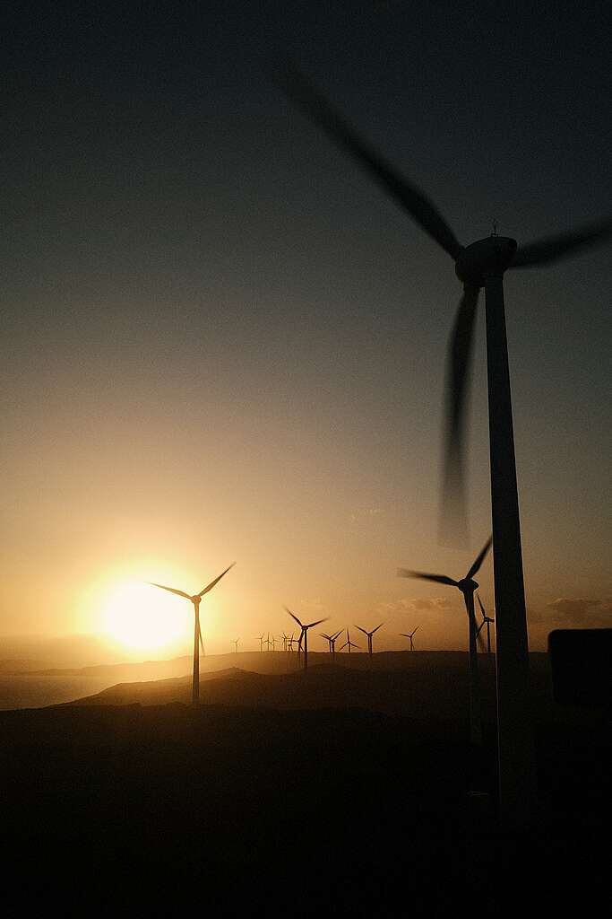 Several wind turbines fade into the distance in the sunset.