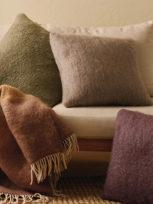 Green, gray, and purple fuzzy pillows and orange blanket handmade by artisans