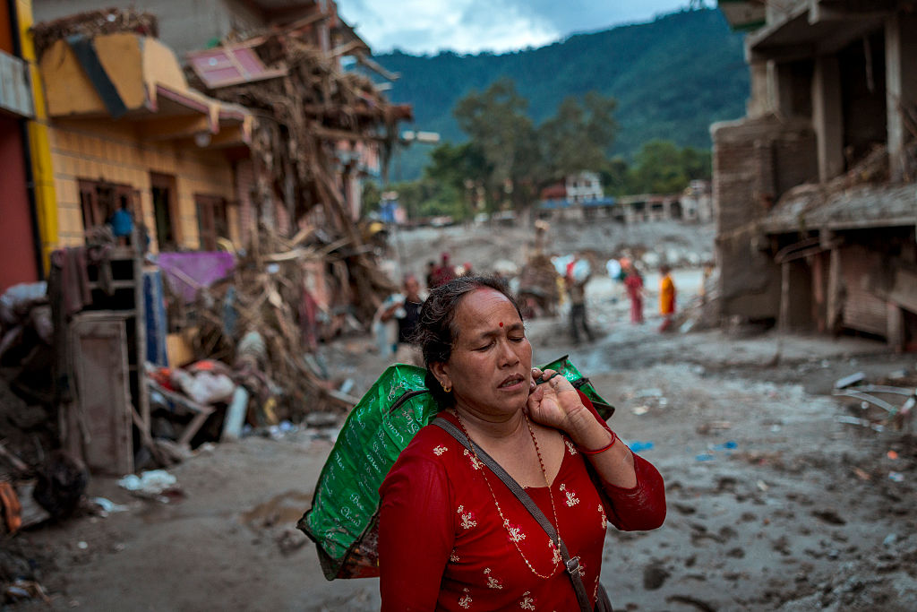 A woman carries belongings recovered from her destroyed home following flash floods in Nepal